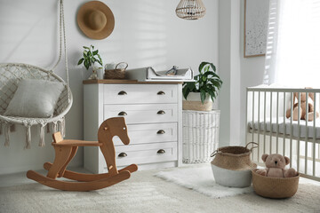 Chest of drawers with changing tray and pad near comfortable cradle in baby room. Interior design