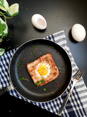 Egg in a hole topped with chili flakes, oregano, and herbs on a pan.