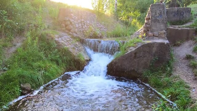 Beautiful sunny waterfall of a mountain river. Old stone bridge with seething water