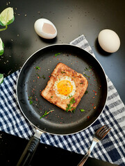 Egg in a hole topped with chili flakes, oregano, and herbs on a pan.