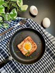 Egg in a hole topped with chili flakes, oregano, and herbs on a pan.