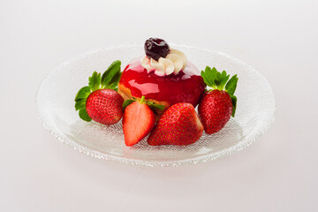 Composition of a glass plate, a donut coated with strawberry syrup, garnished with whipped cream and candied cherries, decorated with fresh strawberries