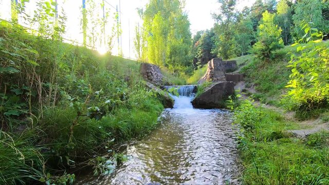 Beautiful sunny waterfall of a mountain river. Old stone bridge with seething water