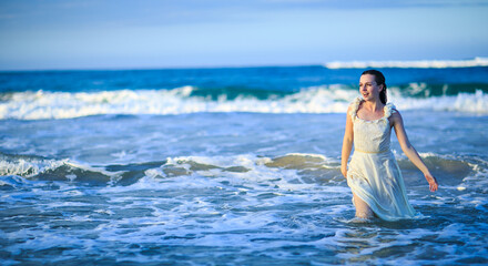 Fototapeta na wymiar girl in wet white dress goes in water at beach. vacation in tropical.