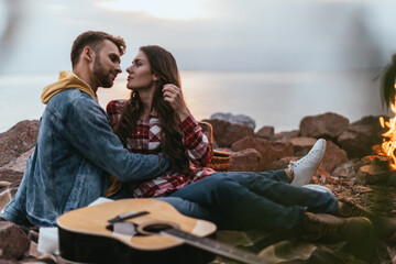 Fototapeta premium selective focus of bearded man hugging girlfriend near acoustic guitar and bonfire
