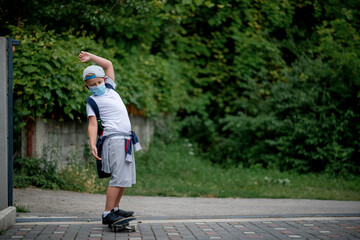 Caucasian Little boy riding a  skateboard wearing a protective face mask because a corona virus