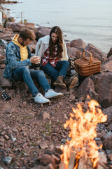 selective focus of couple sitting on stones near bonfire and lake