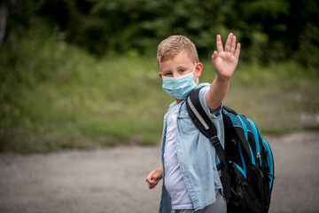 Fototapeta premium Happy little boy with medical mask and backpack on way to school. Healthy adorable child outdoors. Back to school after quarantine time from corona pandemic disease.