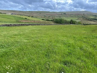 Large open landscape, with meadows, fields, dry stone walls, rising to the hills, above Denholme, Bradford, UK