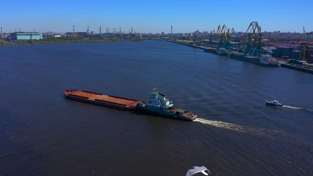 Aerial view of a row of construction or cargo cranes on the river bank with a barge passing by. Ship docks off Kanonersky Island. Industrial port with water barges and transport tugs.
