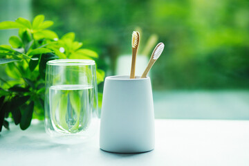 Two bamboo toothbrushes in a cup and glass with water