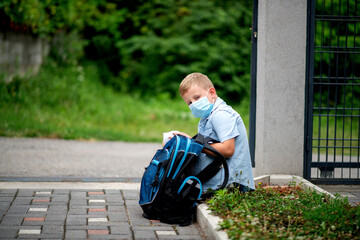 Cute schoolboy studying with protective mask outside