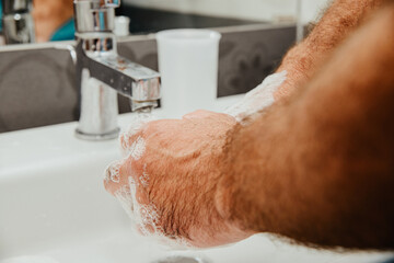 Fototapeta premium The man washes his hands with soap. Concept of caring for personal hygiene. The man is using soap in the bathroom.