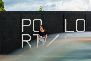 Woman standing in front of a black wall waiting while a car passes in front of the camera in Birmingham, UK.