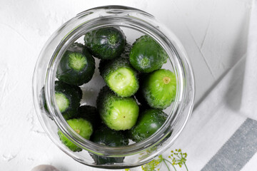 Cornichons in a glass jar ready to be salted on the white table