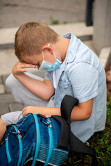 Sad schoolboy studying with protective mask outside