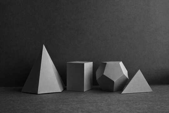 Platonic solids figures geometry. Abstract geometrical figures still life composition. Three-dimensional prism pyramid cube objects on black gray background.