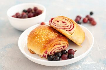 Fresh buns with berry filling decorated with black currants and gooseberry on a light blue concrete background.