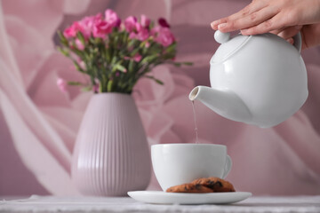 Woman pouring hot tea into cup at table, closeup - Powered by Adobe