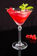 Cold cocktail with red currants in the martini glass on the dark background. Location vertical.