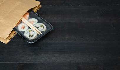 Obraz na płótnie Canvas Sushi tray in paper bag on black wooden background. Copy space.