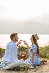 side view of happy couple clinking glasses with red wine while sitting near lake