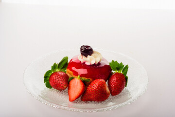 Composition of a glass plate, a donut coated with strawberry syrup, garnished with whipped cream and candied cherries, decorated with fresh strawberries
