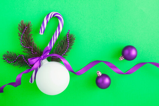 Christmas composition with white ball, branches of spruce and caramel cane on the green background. Copy space.