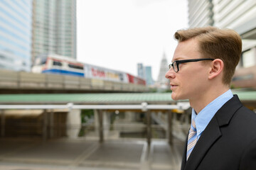 Profile view of young handsome blond businessman with eyeglasses in the city outdoors
