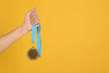 Woman holding bronze medal on yellow background, closeup. Space for design
