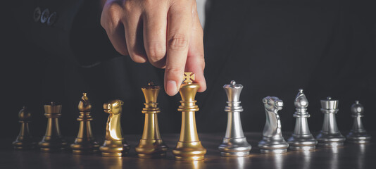 Hand of businessman moving the golden king chess to play successfully in the competition. management or leadership strategy and teamwork concept.