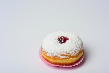 Donut on a pink paper basket on a white background decorated with sugar powder and strawberry jam