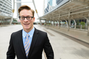 Happy young handsome blond businessman with eyeglasses in the city outdoors