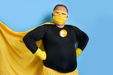 handsome brave strong man has a mad desire, a dream to shield the world from dirt and evil. fat superhero in yellow costume posing isolated over blue background