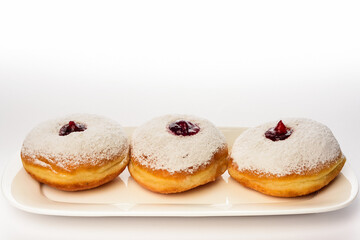 Three donuts on a white plate on a white background decorated with sugar powder and strawberry jam