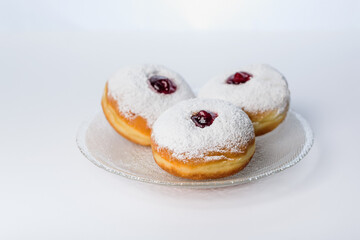 Three donuts on a glass plate on a white background decorated with sugar powder and strawberry jam