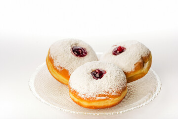 Three donuts on a glass plate on a white background decorated with sugar powder and strawberry jam
