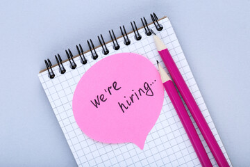 Text We Are Hiring on paper with pencils on grey background