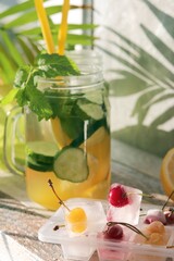 Cold drink of citruses, cucumbers and mint in glass cups, ice with cherries on a wooden table, detox water, home cooking, healthy food