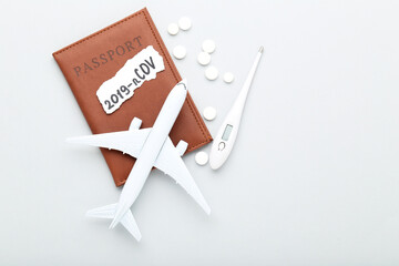 Text 2019-nCov with pills, thermometer, passport and airplane model on grey background