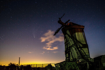 Summer clear night sky with stars and comet C/2020 F3 (NEOWISE) with old abandoned wooden windmill...