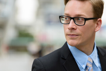 Young handsome blond businessman with eyeglasses thinking in the city outdoors
