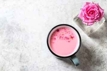 Obraz na płótnie Canvas Ayurvedic rose moon milk. A trendy relaxing form of drink before bed. Milk with rose petals in a gray mug on a light concrete background.