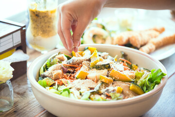 Hand putting parmesan cheese on salad bowl, consisting of steamed pumpkin, boiled egg, biscuits, grilled mushrooms, carrots and lettuce. Concept of healthy and vegetarian food.