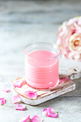 Ayurvedic rose moon milk. A trendy relaxing form of drink before bed. Milk with rose petals on a light concrete background.