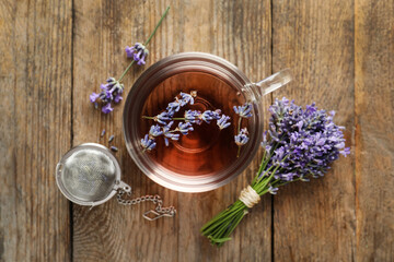 Obraz na płótnie Canvas Fresh delicious tea with lavender, strainer and beautiful flowers on wooden table, flat lay