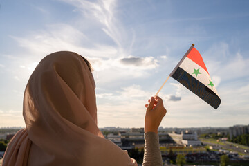 Fototapeta premium Silhouette of muslim woman in head scarf with Syria flag at blue sunset sky. Concept of freedom