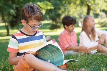 Fototapeta premium Cute little boy studying outdoors with his friends on background