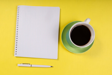 Obraz na płótnie Canvas notepad and a cup of coffee on a yellow background, view from above