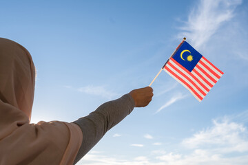 Silhouette of muslim woman in head scarf with Malaysia flag at blue sunset sky. Concept of freedom